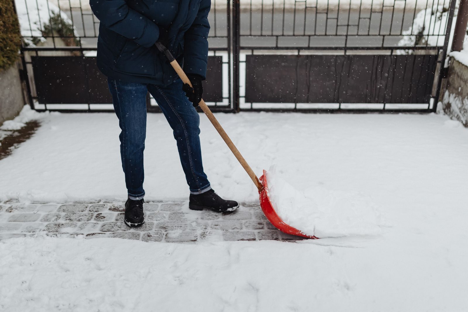 Person clearing snow from a paved driveway with a shovel